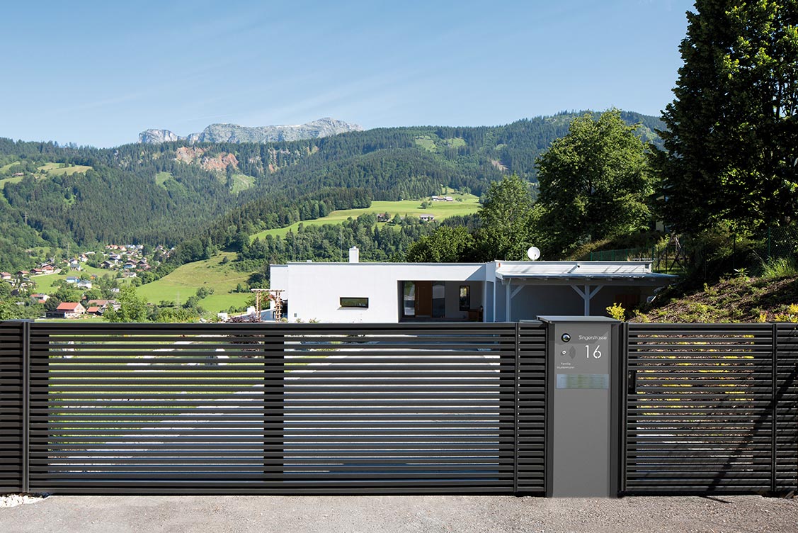 modernes schiebetor mit briefkastensaeule in schwarz vor modernem weissen haus mit aussicht