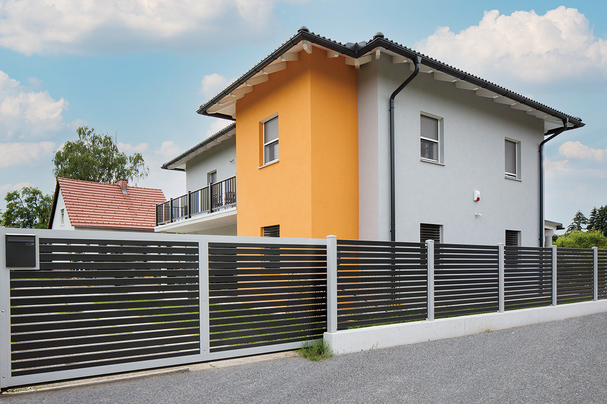 Einfacher Zaun mit Postkasten in Querlatten Optik als Einfahrt mit Haus im Hintergrund