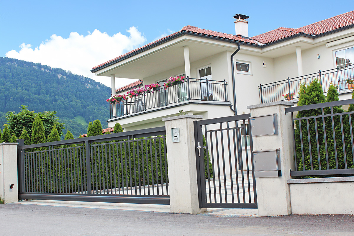 Moderner und stilvoller Zaun aus Aluminium mit Schiebetuer und Gartentuer vor weissem Haus