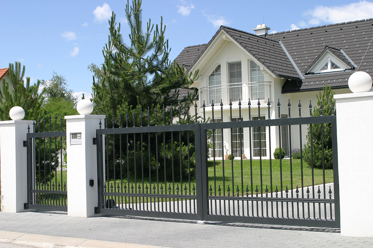 klassisches Fluegeltor elektrisch und Gartentuer vor grossem grünen Garten und weisses grosses Haus