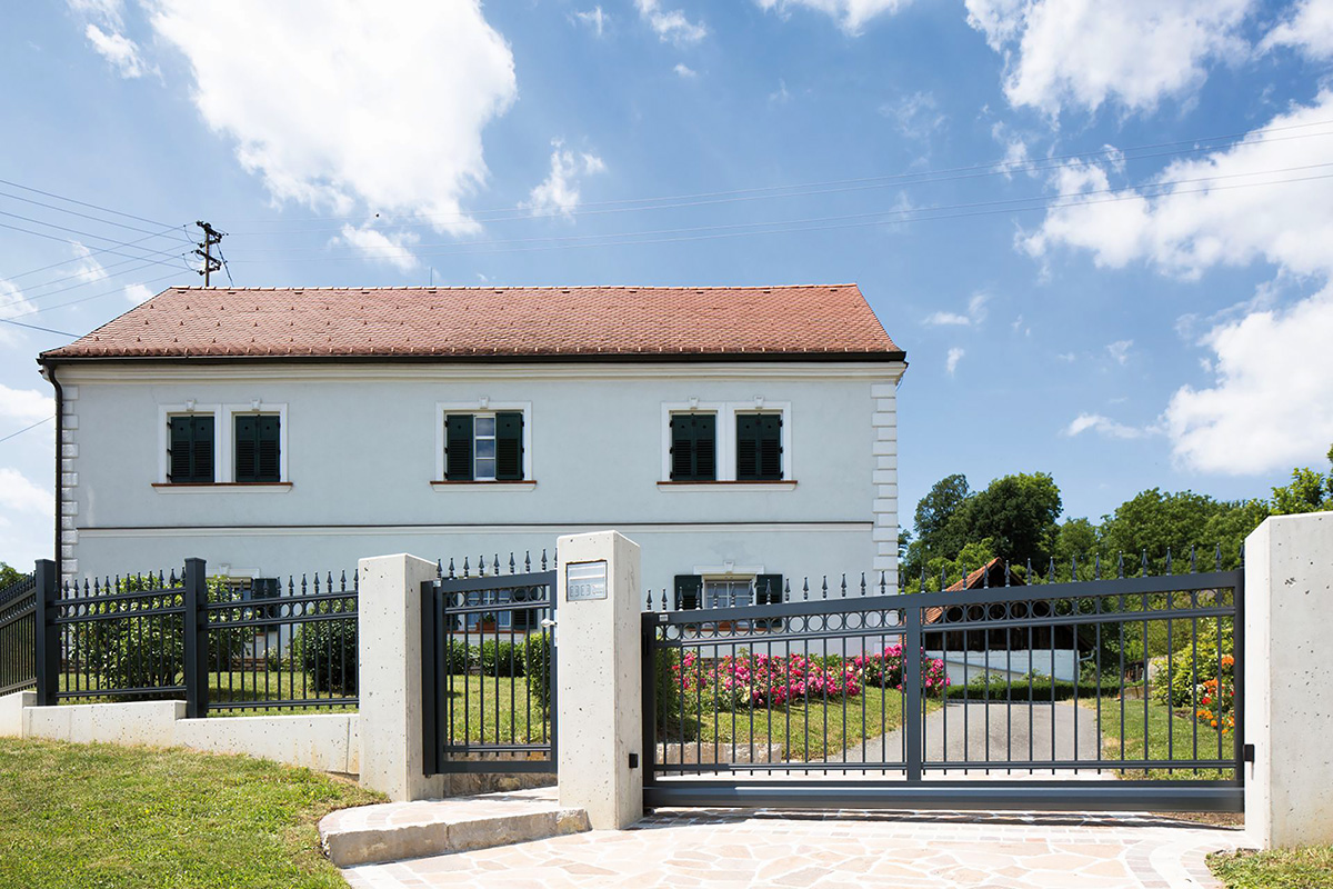 Klassischer Gartenzaun und Gartentuer als Einfahrt vor grossem Garten und Mehrfamilienhaus