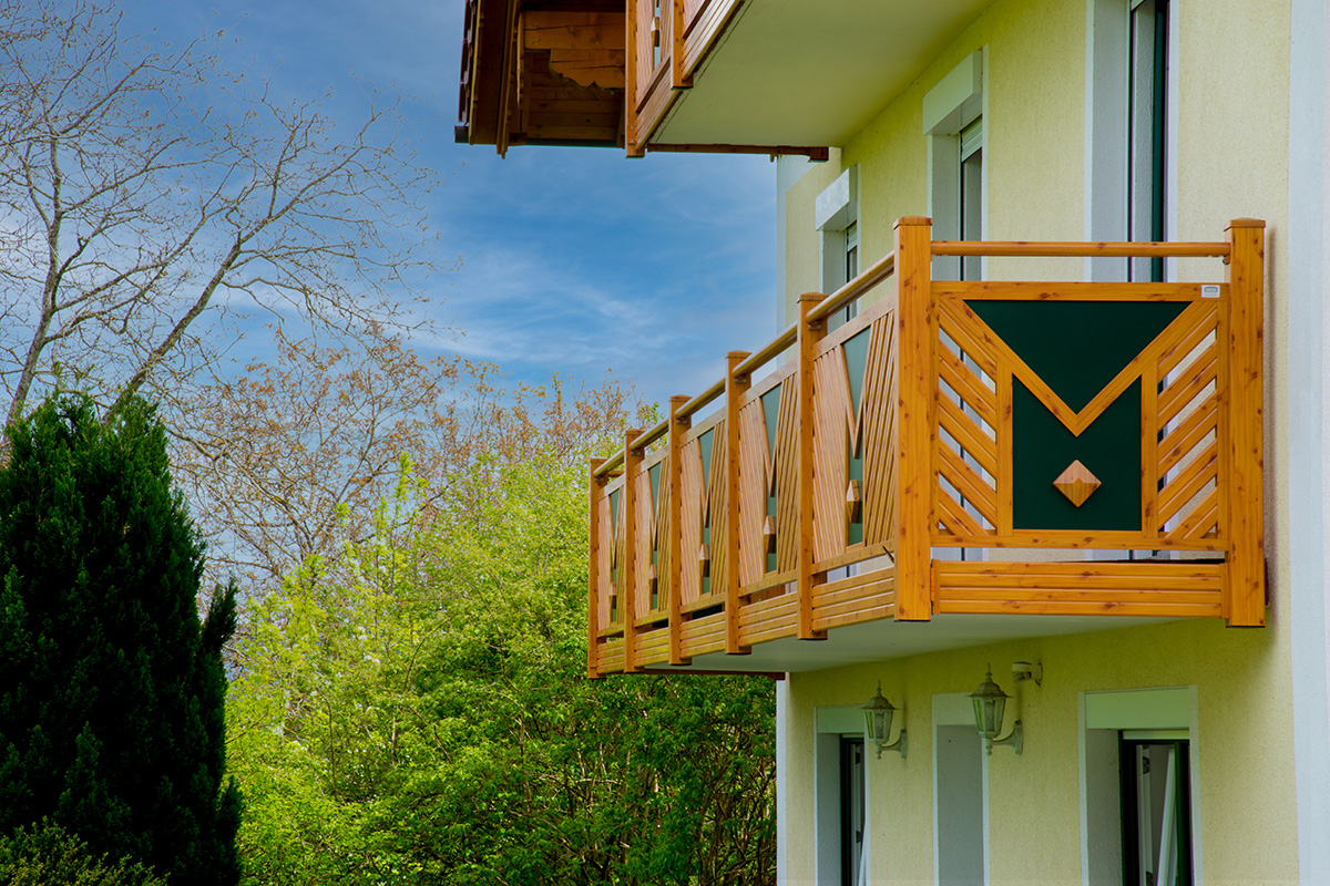 Balkon mit integrierter Dekoraute in Holzoptik an gelbem Haus