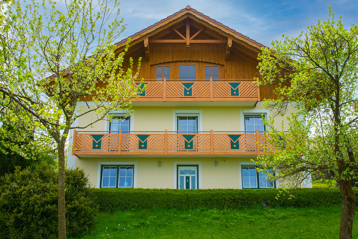 Balkon mit Dreieckselementen in Holzfarbe an gelbem Mehrfamilienhaus in ruhiger Gegend mit Garten
