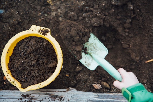 gartenarbeit schaufelt erde in einen gelben kuebel