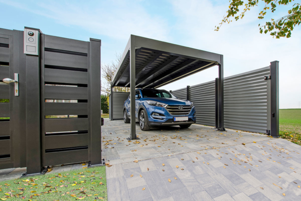 Ein Auto parkt in der Einfahrt unter einem Carport aus Aluminium, dazu passend in der gleichen Farbe ist ein Sichtschutzzaun aus Aluminium in anthrazit zu sehen