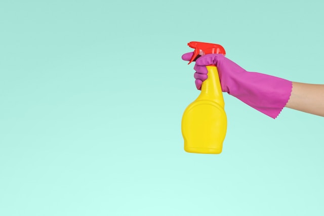 Hand hat pinken Reinigungshandschuh an und hält eine gelbe Reinigungsflasche